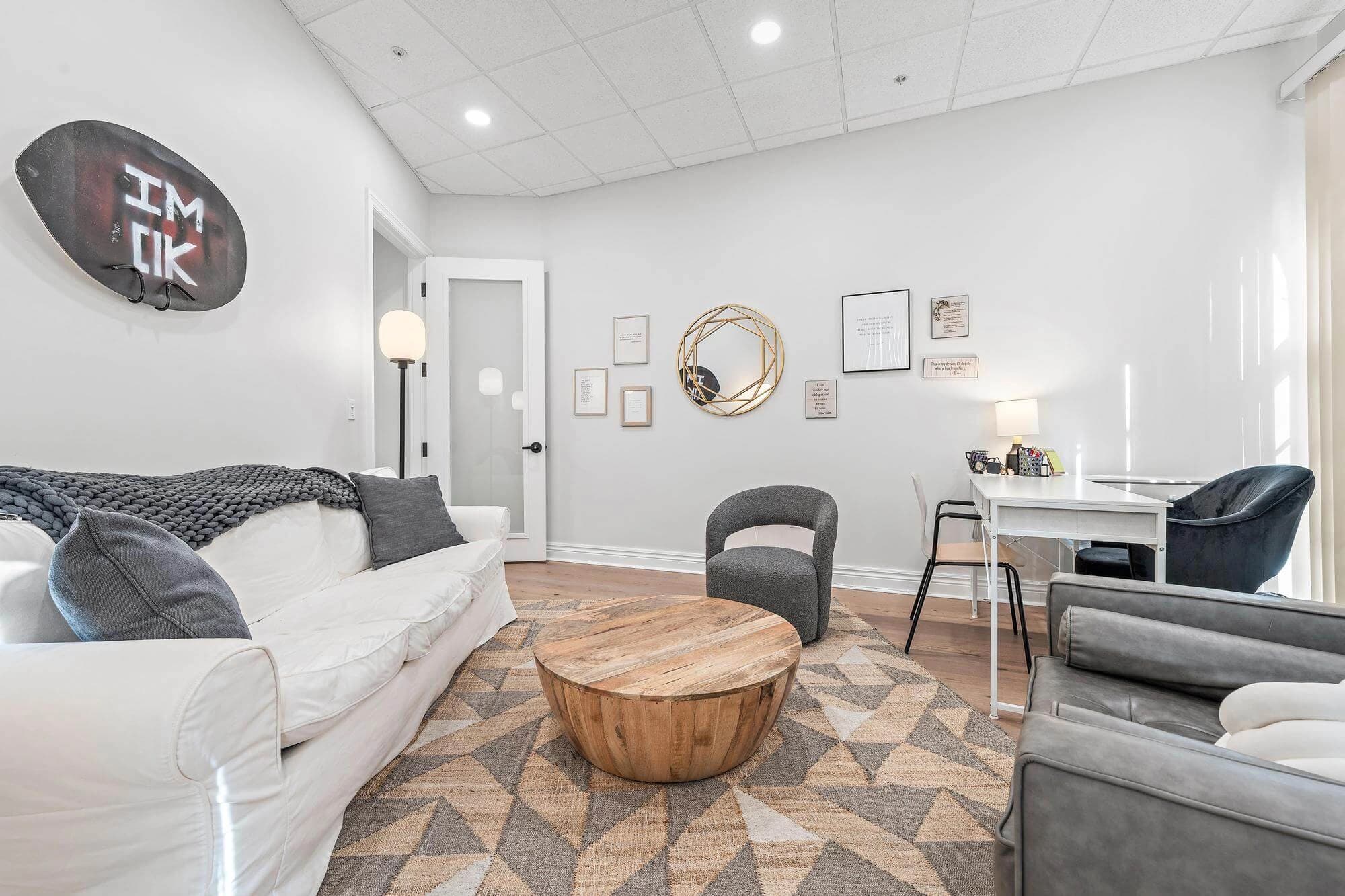 Living-room-style therapy space with white sofa, accent chairs, and warm wood floor